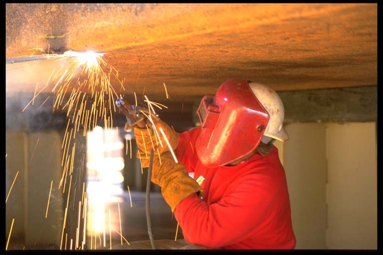 Welder in red gear welding overhead with sparks flying