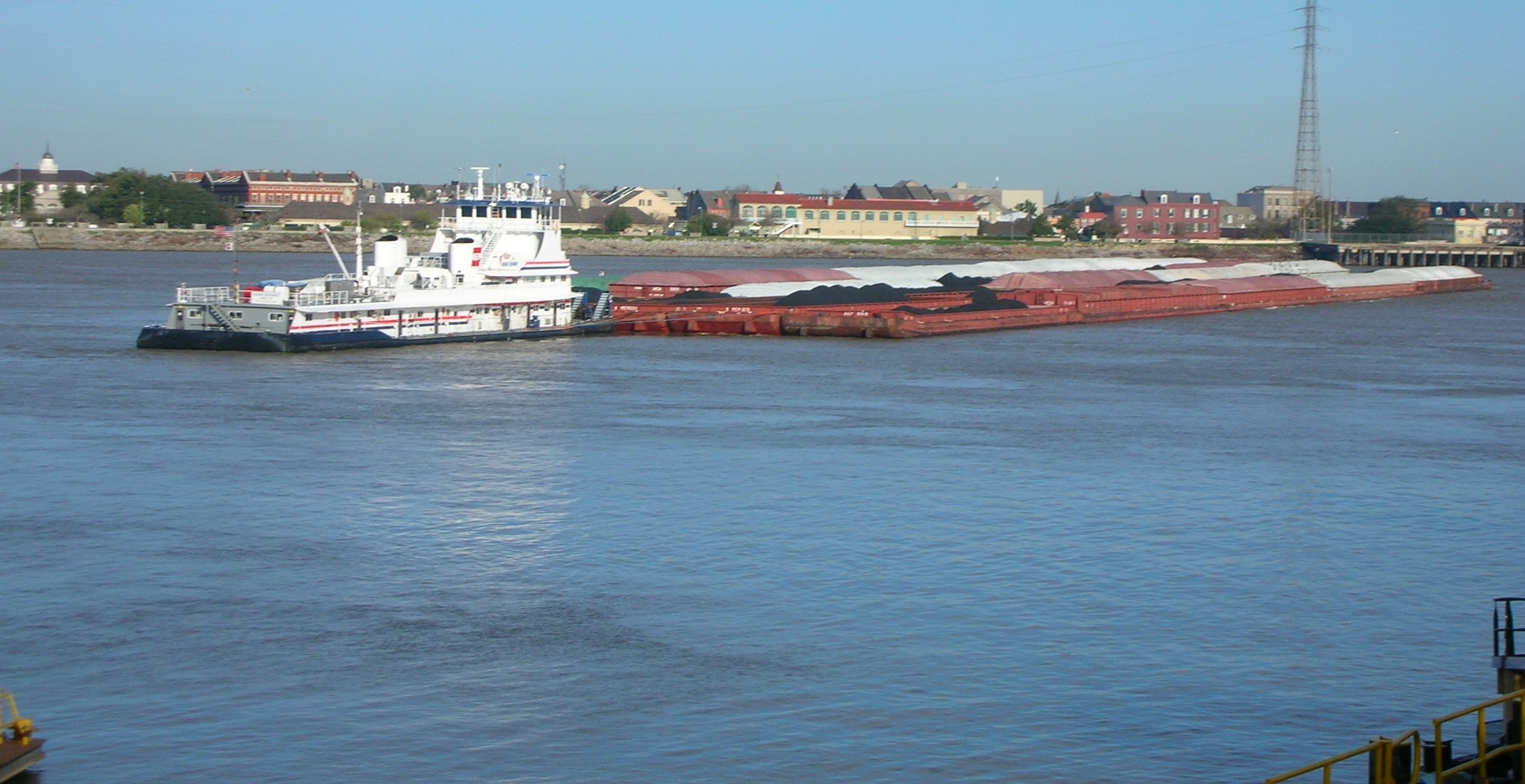 Tugboat pushing loaded coal barges on the Mississippi River with New Orleans skyline in background